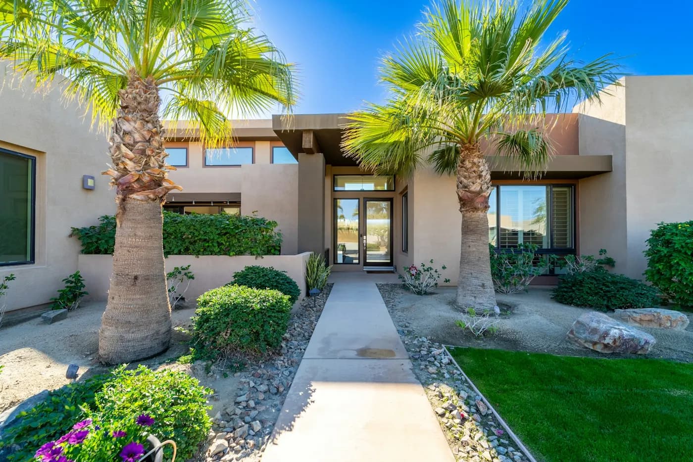 The front walk of a stucco home framed by two palm trees